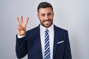 Handsome hispanic man wearing suit and tie showing and pointing up with fingers number three while smiling confident and happy.