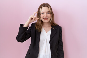 Young caucasian business woman wearing black jacket smiling and confident gesturing with hand doing small size sign with fingers looking and the camera. measure concept.