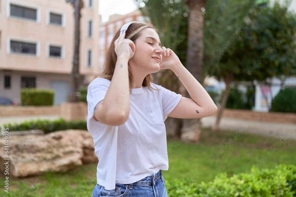 Wall mural Young caucasian woman listening to music at park