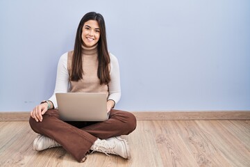 Young brunette woman working using computer laptop sitting on the floor with a happy and cool smile...
