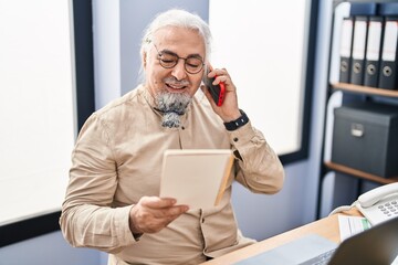 Middle age grey-haired man business worker talking on smartphone reading notebook at office