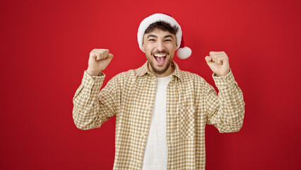 Fototapeta na wymiar Young arab man wearing christmas hat with cheerful expression over isolated red background