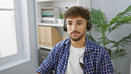 Handsome young arab man, a successful worker, concentrating on his job, wearing a headset indoors at the office. a professional with a relaxed demeanour, providing aid and service for customers.