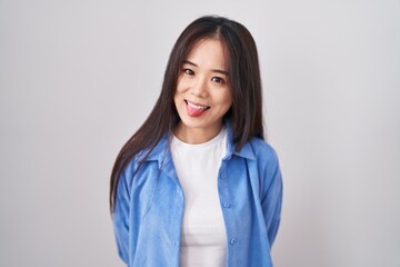Fototapeta premium Young chinese woman standing over white background sticking tongue out happy with funny expression. emotion concept.