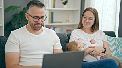 Family of mother, father and baby using laptop sitting on the sofa at home