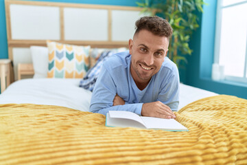 Young hispanic man reading book lying on bed at bedroom