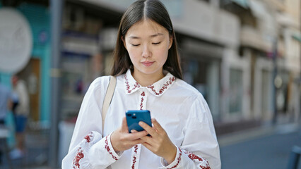 Young chinese woman using smartphone with serious expression at street
