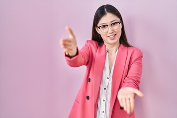 Chinese business young woman wearing glasses looking at the camera smiling with open arms for hug. cheerful expression embracing happiness.
