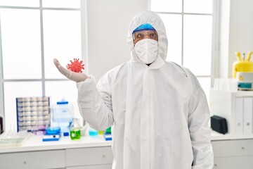 Fototapeta premium Hispanic young man working at scientist laboratory holding virus toy scared and amazed with open mouth for surprise, disbelief face