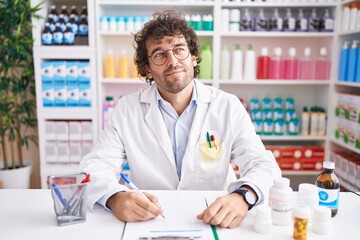 Hispanic young man working at pharmacy drugstore smiling looking to the side and staring away...