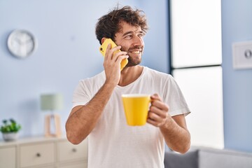 Fototapeta premium Young man talking on smartphone drinking coffee at home