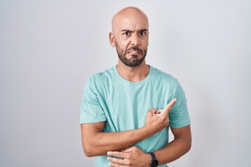 Middle age bald man standing over white background pointing aside worried and nervous with...