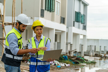 Foreman man and woman with Yellow helmet holding laptop in constuction site