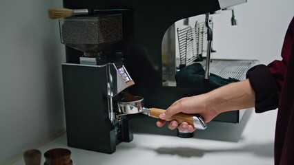 Barista pouring ground coffee in portafilter close up. Man hand holding filter.