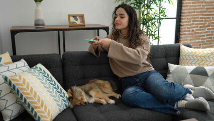 Young hispanic woman with dog make photo by smartphone to asleep dog at home