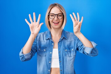 Young caucasian woman standing over blue background showing and pointing up with fingers number...