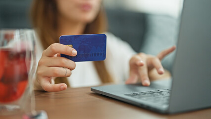 Young beautiful hispanic woman shopping with laptop and credit card sitting on floor at home