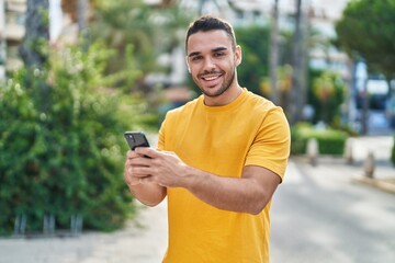 Young hispanic man smiling confident using smartphone at street