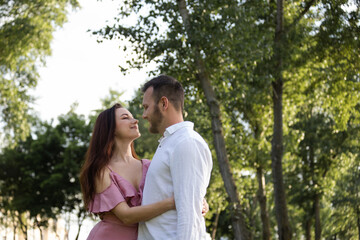 Fototapeta premium Lovely couple hugging in park. Portrait of attractive young cheerful pair lovers relaxing on summer forest background. Sweet family embracing outdoors. Charming spouses anniversary at picnic
