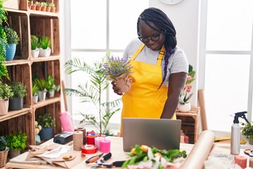 African american woman florist using laptop holding plant at florist