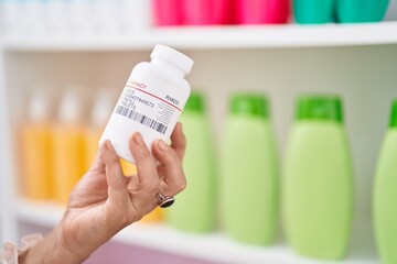Middle age grey-haired woman customer holding pills bottle at pharmacy