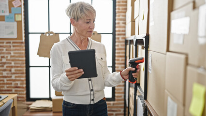 Middle age blonde woman ecommerce business worker scanning packages at office