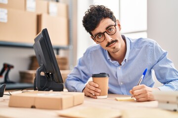 Young caucasian man ecommerce business worker drinking coffee writing on reminder paper at office