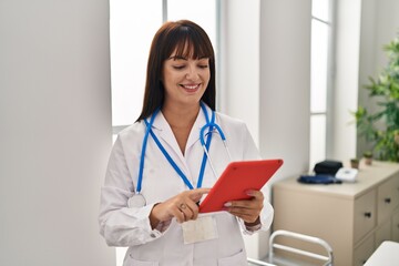 Young beautiful hispanic woman doctor smiling confident using touchpad at clinic