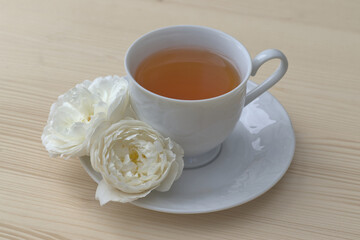 Rose petals tea with white rose in a white tea cup on the saucer top view with a copy space. On wooden table. Herbal drink alternative medicine concept.