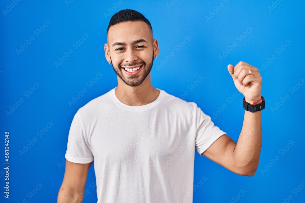 Poster Young hispanic man standing over blue background dancing happy and cheerful, smiling moving casual and confident listening to music