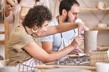 Woman decorating a ceramic vase while having a pottery class. Hobby and craft concept. - obrazy, fototapety, plakaty