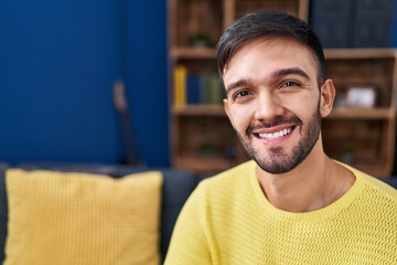 Fototapeta premium Young hispanic man smiling confident sitting on sofa at home