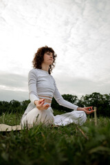 Peaceful young yogi woman sitting in lotus pose at city park landscape background. Girl doing yoga...