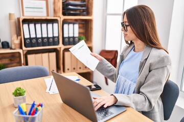 Young beautiful hispanic woman business worker using laptop reading document at office