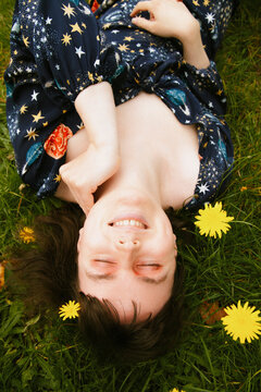 Happy young woman lying in grass and flowers eyes closed
