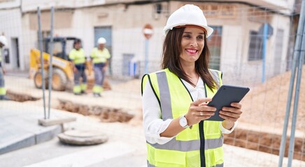 Young beautiful hispanic woman architect using touchpad at street