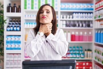 Middle age brunette woman working at pharmacy drugstore shouting and suffocate because painful...
