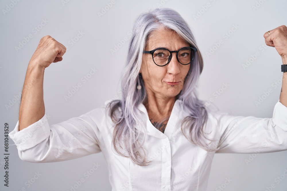 Wall mural middle age woman with tattoos wearing glasses standing over white background showing arms muscles sm