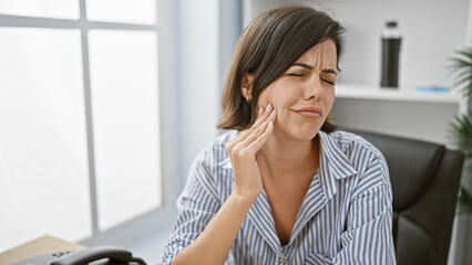 Young hispanic woman, a successful businesswoman in her office, suffering severe toothache while...