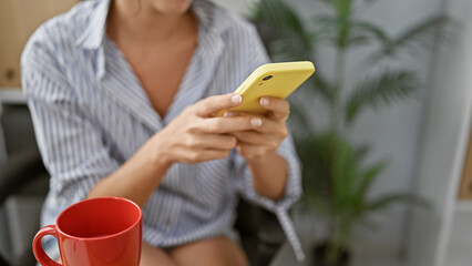 Hands of successful hispanic woman worker typing a message on her phone, engrossed in work at her...