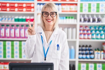 Young caucasian woman working at pharmacy drugstore showing and pointing up with fingers number two...