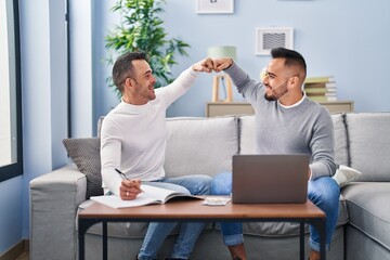 Two men bump fists sitting on sofa at home