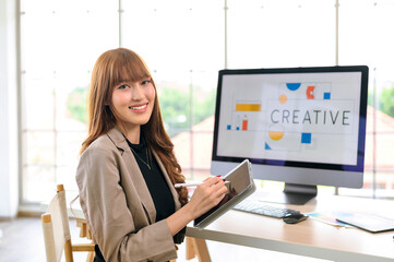 Asian female artist drawing something on graphic tablet. graphic designer working at office. Looking at camera.