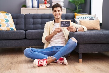 Young hispanic man holding blackboard with new home text looking positive and happy standing and...