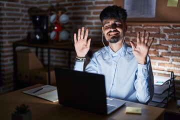 Young hispanic man with beard working at the office at night showing and pointing up with fingers number ten while smiling confident and happy.