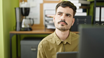 Young hispanic man business worker using touchpad thinking at office