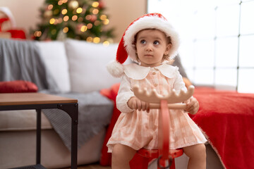 Adorable caucasian girl playing with reindeer rocking by christmas tree at home