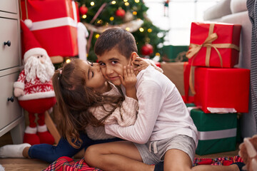 Brother and sister kissing and hugging each other sitting on floor by christmas gifts at home