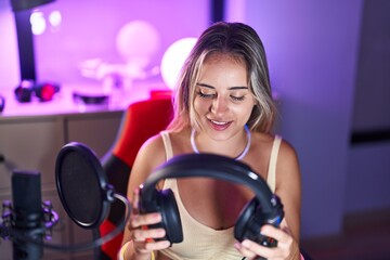 Obraz premium Young blonde woman streamer smiling confident holding headphones at gaming room
