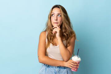 Young woman with strawberry milkshake isolated on blue background having doubts and thinking